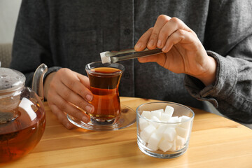 Woman adding sugar cube into aromatic tea at wooden table, closeup