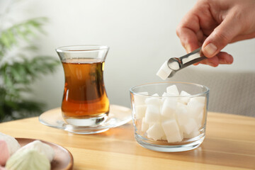 Woman adding sugar cube into aromatic tea at wooden table indoors, closeup