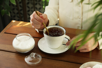 Woman stirring sugar in tea at wooden table indoors, closeup