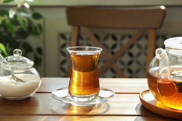 Aromatic tea in glass, teapot and sugar on wooden table indoors