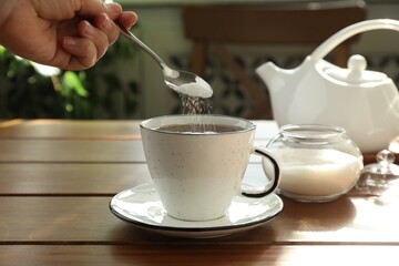 Woman adding sugar into aromatic tea at wooden table indoors, closeup