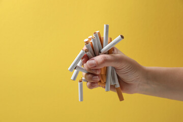 Stop smoking. Woman holding whole and broken cigarettes on yellow background, closeup. Space for...