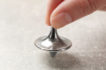 Woman playing with metal spinning top at grey textured background, closeup
