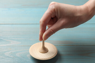 Woman playing with spinning top at light blue wooden table, closeup