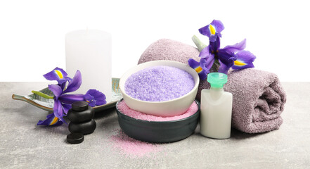 Different types of sea salt, rolled towel, spa stones, candle and flowers on grey table against...