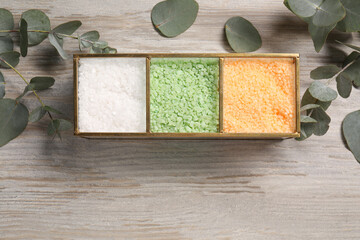 Different types of sea salt and eucalyptus branches on wooden table, flat lay. Space for text