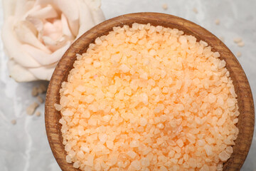 Orange sea salt in bowl and rose on grey table, top view