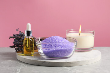 Violet sea salt in bowl, lavender flowers, burning candle and cosmetic product on grey marble table