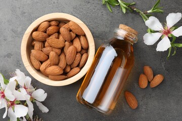 Almond oil in bottle, flowers and nuts on grey textured table, flat lay