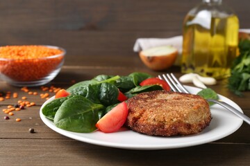 Tasty fried vegetarian cutlet served with spinach and tomato on wooden table, closeup