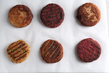 Different tasty vegetarian cutlets on parchment paper, flat lay