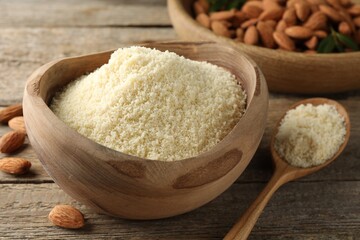 Fresh almond flour in bowl, spoon and nuts on wooden table, closeup