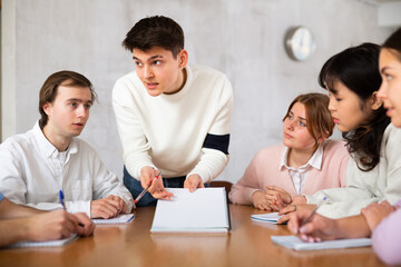 Positive motivated young guy, student team leader holding meeting with group, explaining details of...
