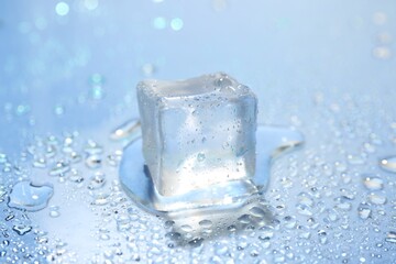 Melting ice cube and water drops on light blue background, closeup