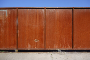 Rundown heavily weathered and rusted reddish colored roll aside door on small wheels and track