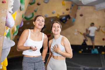 Two young female friends standing in training area of climbing gym and discussing possibility of...