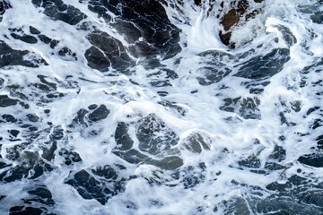 Close-up view of the patern of white foam with small bubbles on the surface of moving ocean water....