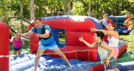 Laughing adult man having funny competition in collect of hoops on inflatable trampoline in summer...