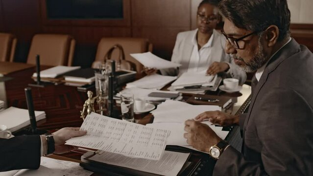 Side pull out footage of team of diverse lawyers gathered in conference hall analyzing civil or criminal case looking through documentary evidence during meeting