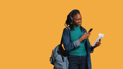 African american woman taking picture of school homework to send to colleague, listening music, studio background. Student photographing papers with information needed for exam, camera B