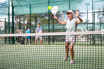 Caucasian elderly woman in sleeveless shirt playing padel tennis match during training on court.