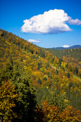 Fototapeta premium Large white cloud in the blue sky, mountain landscape on a sunny autumn day. Mountains, hills in the fall. Vertical photo of the nature reserve.