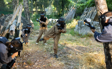 Group of men and women in protective clothes and helmets shooting with paintball markers. Teams...