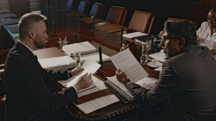 Side footage of attorney presenting legal document to law firm manager who comparing two copies during meeting in conference hall