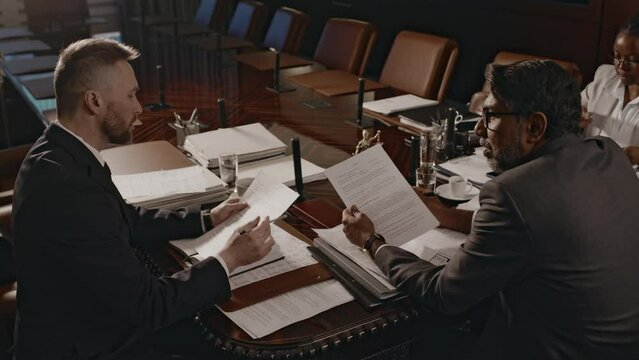 Side footage of attorney presenting legal document to law firm manager who comparing two copies during meeting in conference hall