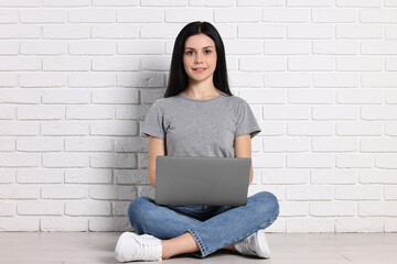 Student with laptop sitting on floor near white brick wall