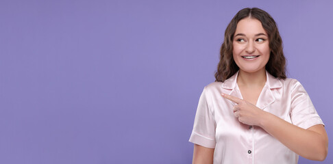 Smiling woman with braces pointing at something on violet background. Banner design with space for...