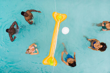 Overhead of happy diverse friends playing fun game of volleyball in sunny swimming pool, copy space