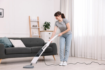 Happy young housewife cleaning floor with steam mop at home