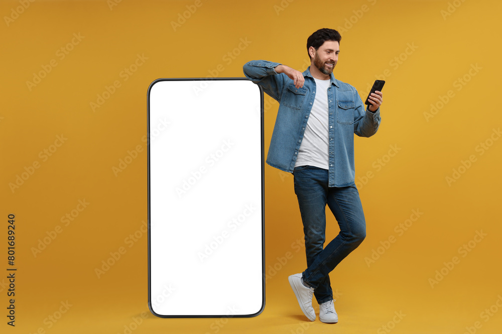 Poster man with mobile phone standing near huge device with empty screen on orange background. mockup for d