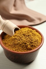 Curry powder in bowl and scoop on white table, closeup