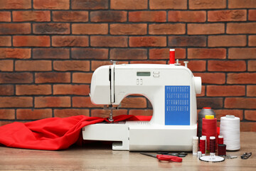 Sewing machine with fabric and craft accessories on wooden table against brick wall