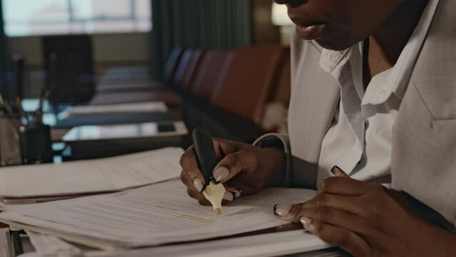 Side tilt closeup of concentrated African American attorney in suit and glasses highlighting relevant information in paperwork or documentary evidence sitting in boardroom during workday