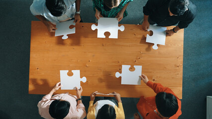 Top down view of skilled business people assemble jigsaw puzzle on meeting table. Group of diverse...