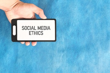 Social media ethics concept. Human hand holding mobile phone on blue background.