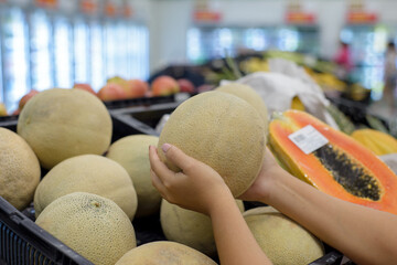 Female hands picking up a melon from a shelf in the supermarket.