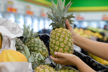 Female hands picking up a pineapple from a supermarket shelf.