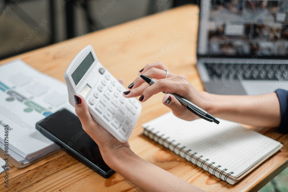 Poster close-up of a professional's hands using a calculator and taking notes, with a laptop and smartphone