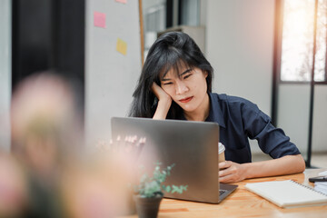 Contemplative businesswoman with a thoughtful expression working on her laptop at a desk with notes and a coffee cup.