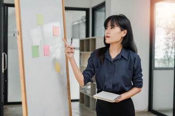 Businesswoman using sticky notes for brainstorming and organizing tasks on a whiteboard in a bright office space.