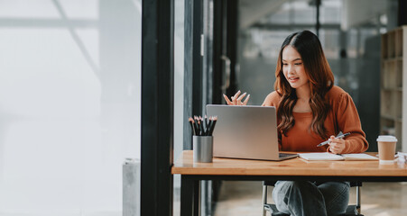 Young businesswoman looks animated and engaged while speaking during a video conference call on her laptop in a stylish workspace.