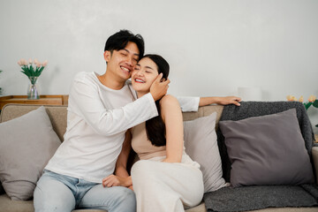 Joyful couple shares a tender moment, laughing and embracing on a cozy sofa in a warmly decorated living room.