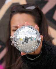 A young woman holding a disco ball in front of her face