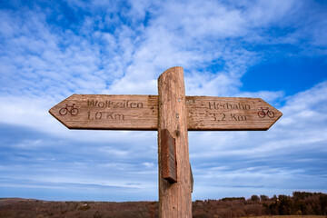 Wooden directional sign showing direction for cycling, in nature park, with blue sky