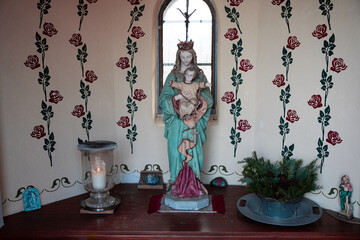 a statue of a woman and a baby in front of a window with a flowered wallpaper.