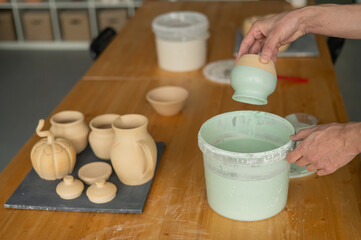 Close-up of a potter's hands glazing a pottery piece. 